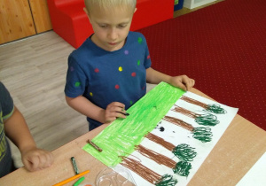Chłopiec ubrany w koszulkę w kropki rysuje obrazek wokół centralnie umieszczonej na nim kropki